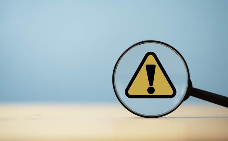 Yellow triangle caution warning sign inside of magnifier glass on blue background